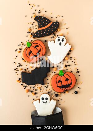 Verschiedene Halloween Lebkuchenkekse - Jack O'Lanterns, schwarzer Hut, Geister, Fledermaus und Zucker streut aus Papiertüte auf beigem Hintergrund. Hallo Stockfoto