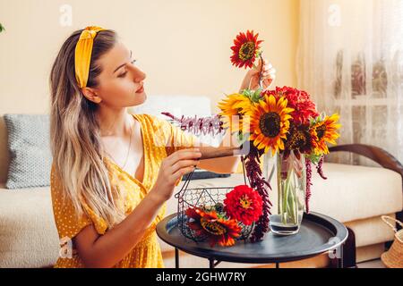 Bouquet Arrangement. Frau stellt Sonnenblumen und Zinnien in Vase zu Hause. Frische Herbstblüten. Innen Stockfoto