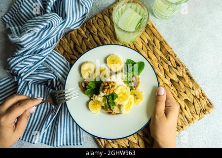 Frau, die ein Stück selbstgemachten Banane, Walnuss und Minzkäsekuchen mit einem Glas Gurkenwasser isst Stockfoto