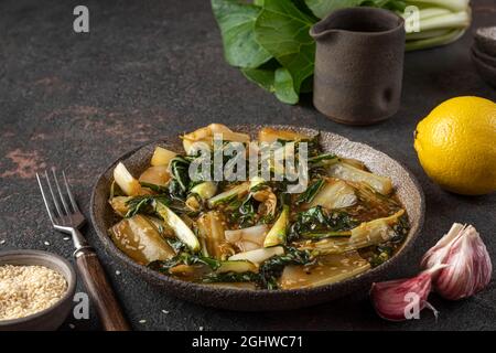 Bok Choy Gemüse unter Rühren braten mit Sojasauce und Sesam auf dunklem Hintergrund. Chinesische Küche. Gesundes veganes Essen. Nahaufnahme Stockfoto