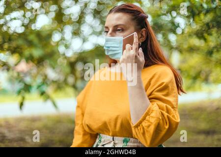 Kaukasische Erwachsene Frau, die eine schützende medizinische Maske im Stadtpark abzieht. Wir haben gewonnen. Keine Quarantäne mehr. Stockfoto