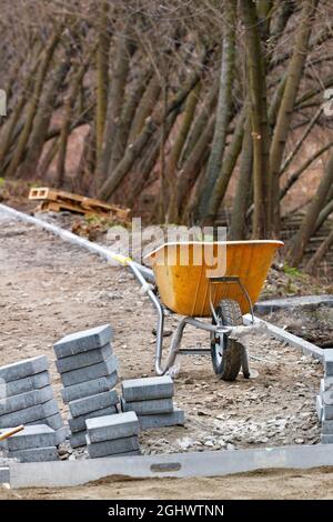 Alte gelbe Konstruktion Schubkarre vor dem Hintergrund eines Stapels von Pflasterplatten. Vertikales Bild. Stockfoto