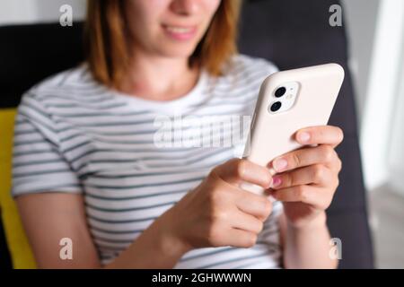 Eine fröhliche Frau nutzt ihr Smartphone, das auf dem Sofa liegt. Freiberuflich oder als Blogger zu Hause arbeiten. Lesen von Büchern auf dem Smartphone Stockfoto