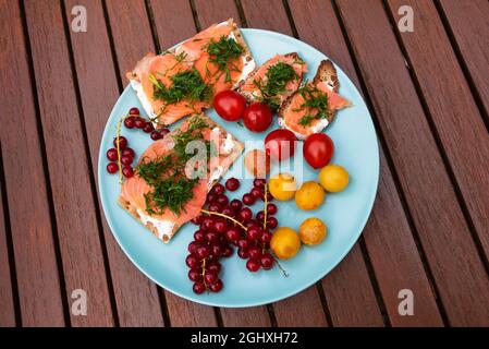 Bunte gesunde leichte Mahlzeit im Freien, während Sie von zu Hause aus arbeiten. Fettarme Bio-Forellen-Sandwiches mit knuspriges Brot, Kirschtomaten und gelben Pflaumen der Saison Stockfoto