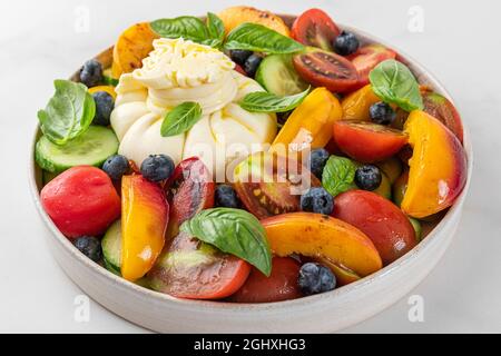 Frischer Salat mit gegrillten Pfirsichen, Burrata-Käse, Heidelbeeren, Gemüse und Basilikum auf einem Teller auf weißem Hintergrund. Nahaufnahme. Gesunde Ernährung Sommer Essen Stockfoto