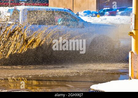 Fahrzeuge, die durch stehendes Wasser von der Schneeschmelze fahren und schlammiges Spray erzeugen. Stockfoto