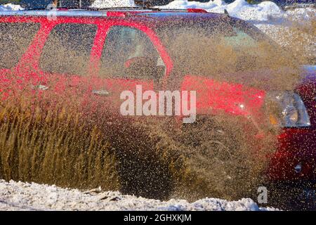 Fahrzeuge, die durch stehendes Wasser von der Schneeschmelze fahren und schlammiges Spray erzeugen. Stockfoto