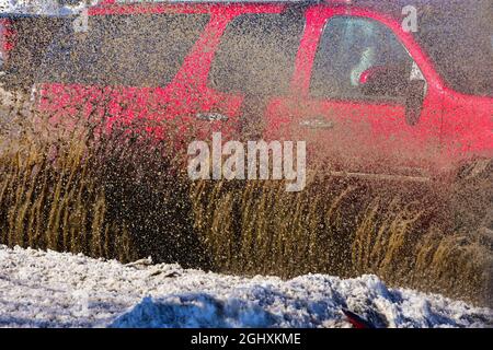 Fahrzeuge, die durch stehendes Wasser von der Schneeschmelze fahren und schlammiges Spray erzeugen. Stockfoto