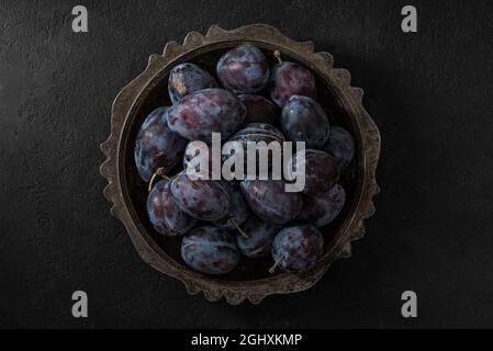 Frische reife blaue Pflaumen in einer Schüssel auf schwarzem Hintergrund. Draufsicht. Low key Stockfoto