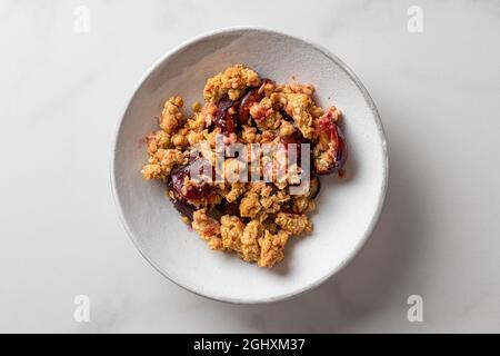 Plum Crumble Dessert auf einem Teller auf weißem Hintergrund für leckeres Frühstück. Draufsicht Stockfoto