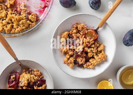 Leckeres Frühstück. Plum Crumble Dessert in Tellern mit Löffeln und Teetasse mit Zitrone auf weißem Hintergrund. Draufsicht Stockfoto