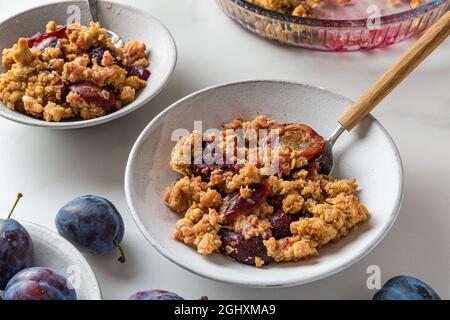 Plum Crumble Dessert in Tellern mit Löffeln auf weißem Hintergrund für leckeres Frühstück. Nahaufnahme Stockfoto