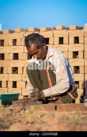 TIKAMGARH, MADHYA PRADESH, INDIEN - 11. AUGUST 2021: Indischer Mann, der mit einem Schimmel und nassem Lehm von Hand Hausziegel anstellt. Stockfoto