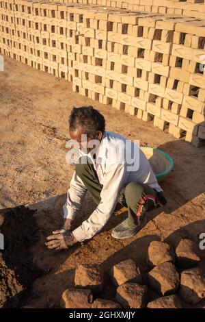 TIKAMGARH, MADHYA PRADESH, INDIEN - 11. AUGUST 2021: Indischer Mann, der mit einem Schimmel und nassem Lehm von Hand Hausziegel anstellt. Stockfoto