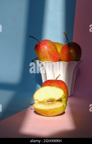 Schuss von Äpfeln in einem kleinen weißen Keramiktopf und auf der rosa und blauen Oberfläche Stockfoto