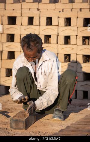 TIKAMGARH, MADHYA PRADESH, INDIEN - 11. AUGUST 2021: Indischer Mann, der mit einem Schimmel und nassem Lehm von Hand Hausziegel anstellt. Stockfoto