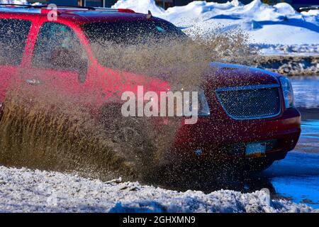 Fahrzeuge, die durch stehendes Wasser von der Schneeschmelze fahren und schlammiges Spray erzeugen. Stockfoto