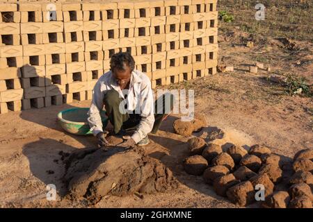 TIKAMGARH, MADHYA PRADESH, INDIEN - 11. AUGUST 2021: Indischer Mann, der mit einem Schimmel und nassem Lehm von Hand Hausziegel anstellt. Stockfoto