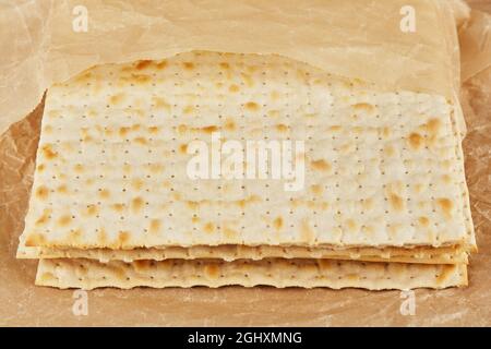 Jüdische koschere Matza für den religiösen Feiertag des Passahfestes auf einem Holztisch, der in ein gelbes Blatt Papier gehüllt ist Stockfoto