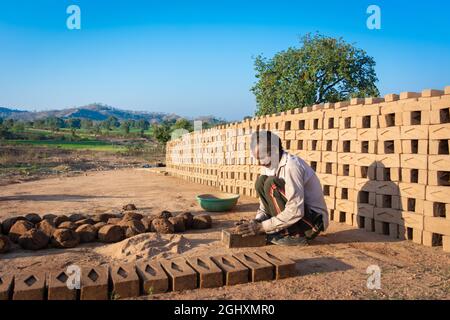 TIKAMGARH, MADHYA PRADESH, INDIEN - 11. AUGUST 2021: Indischer Mann, der mit einem Schimmel und nassem Lehm von Hand Hausziegel anstellt. Stockfoto