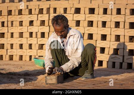 TIKAMGARH, MADHYA PRADESH, INDIEN - 11. AUGUST 2021: Indischer Mann, der mit einem Schimmel und nassem Lehm von Hand Hausziegel anstellt. Stockfoto