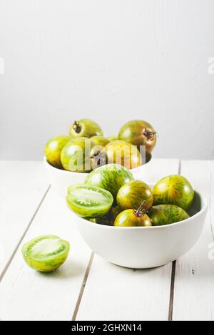 Gestreifte grüne Zebratomaten in einer Schüssel auf einem weißen Holztisch. Stockfoto