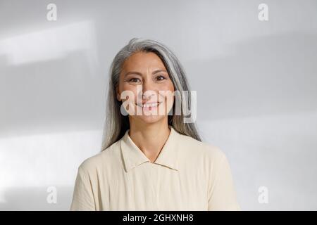 Porträt einer ziemlich grauhaarigen Frau in beiger Bluse auf hellem Hintergrund Stockfoto