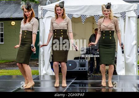 Manhattan Dolls singen in England bei einer militärischen Wiederbelebung Veranstaltung. Sängerinnen aus Amerika besuchen Großbritannien und treten im Regen in USAAF-Uniformen auf Stockfoto