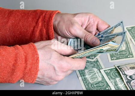 Kaukasische Hände zählen Dollar-Banknoten auf grauem Hintergrund. Männlich hält Geld Währung der Vereinigten Staaten. Nahaufnahme. Selektiver Fokus. Stockfoto