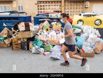 Joggerin läuft an Müll vorbei, der sich neben vollen kommunalen Recyclingbehältern auf der Straße in Spanien stapelt Stockfoto