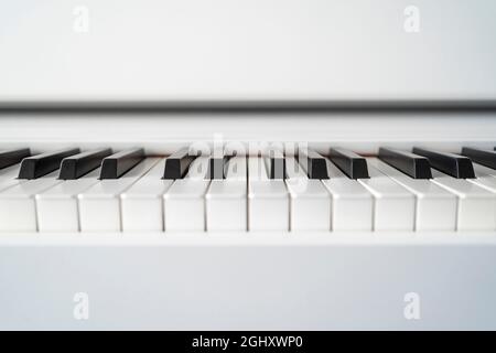 Digitales Klavier, das über die Tasten schaut. Geringe Schärfentiefe. Klassische Musik auf elektronischem Digitalpiano. Schöne Klaviertasten aus nächster Nähe. Stockfoto