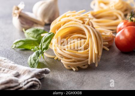 Italienische Nudelnest, Basilikum, Knoblauch und Tomaten. Ungekochte Spaghetti nisten auf dem Küchentisch. Stockfoto
