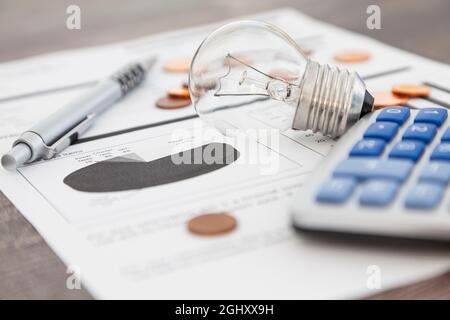 Eine Glühbirne, ein Stift, ein Rechner und einige kupferne Eurocent-Münzen liegen auf einer Stromrechnung. Stockfoto