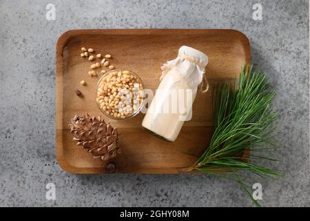 Vegane Zedernmilch in der Flasche in Holzschale auf grauem Hintergrund. Vegetarisches Getränk auf pflanzlicher Basis. Blick von oben. Stockfoto