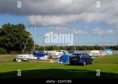 Die Boote vertäuten auf Malthouse Broad am Kai von Ranworth, Norfolk, England, bei Sonnenschein, aber mit bedrohlichen Wolken darüber Stockfoto