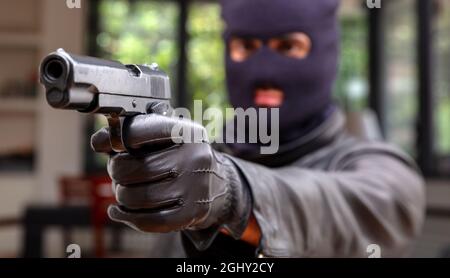Der skrupellose Mörder mit dem Handfeuerkonzept. Verwischter, mit Kapuze bewaffneter Mörder zielt mit einem Geschützrohr, das auf das Opfer gerichtet ist. Mann in schwarzer Balaklava hält Pist Stockfoto