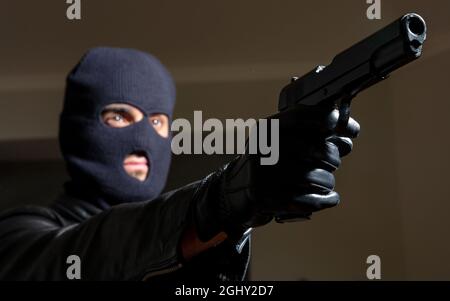 Mörder mit Balaclava-Konzept. Blur kriminellen Mann in schwarzer Kapuze Lederjacke hält Waffe in Handschuhen. Beschlossen, den Aktionsplan „bewaffnete kille“ umzusetzen Stockfoto
