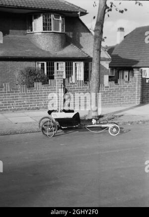 1960s, historisch, ein selbstgemachter Go-Cart der Zeit, geparkt auf einer Vorstadtstraße, England, Großbritannien. Eine DIY-Maschine, die aus alten Holzstücken hergestellt wurde, die an Kinderwagenrädern befestigt und mit einem Stück Seil gesteuert wurden, war ein beliebtes Spielobjekt für Jungen in den späten 50er/frühen 60er Jahren, als sie allgemein als „Trolleys“ bekannt waren. Stockfoto