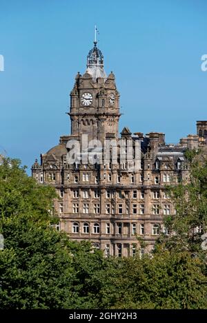 Der Uhrturm des Balmoral Hotels, durch die Bäume in den Princes Street Gardens, Edinburgh, Schottland, Großbritannien. Stockfoto