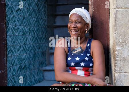 Eine Frau mit einer amerikanischen Flaggenweste sitzt an der Straße in Havanna, Kuba. Stockfoto
