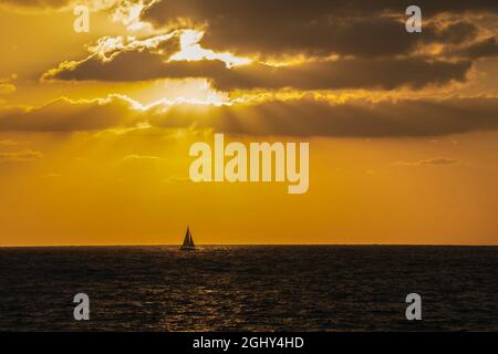 Ein Segelboot auf See, wenn die Sonne zum Horizont hin untergeht. Stockfoto