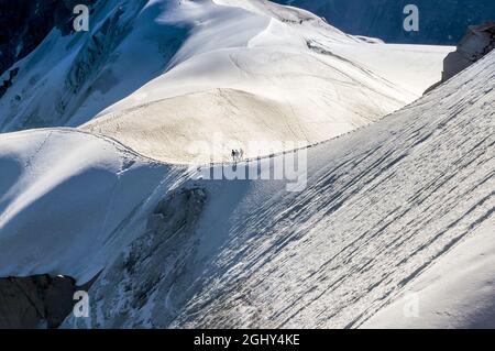 Die Berge der französischen Alpen bieten einen Panoramablick mit Silhouetten von Bergsteigern als Seilschaft, die auf dem verschneiten Hang unter der Aiguille du Midi 3842m absteigt. Beau Stockfoto