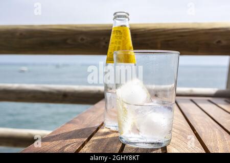 Flasche und Glas Wasser mit einer Scheibe Zitrone und Eis auf einem Holztisch Stockfoto