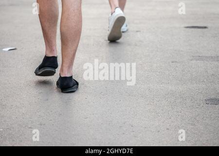 Bild von den Füßen eines weißen kaukasischen Mannes, der Flip-Flop-Sandalen und -Socken trägt, der auf einer Straße im Freien läuft. Stockfoto