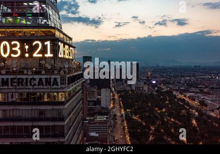 Luftaufnahme von Finanzhochhäusern, die die Zeit auf digitaler Uhr an der Ecke des Gebäudes in Mexiko-Stadt bei Nacht unter bewölktem Himmel anzeigen Stockfoto