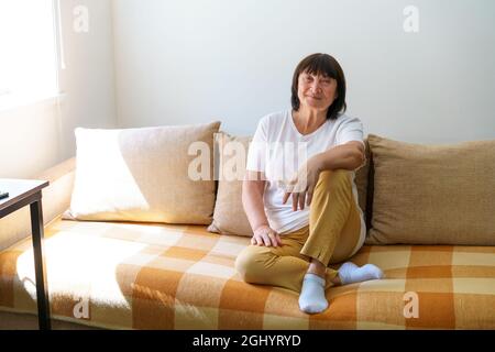 Portrait im Kopf einer friedlichen, ruhigen Frau mittleren Alters, die sich allein zu Hause auf dem gemütlichen Sofa entspannt. Nette glückliche 60s alte reife Großmutter, die sich auf der Wohnzimmercouch entspannt, die für Fotos posiert. Stockfoto