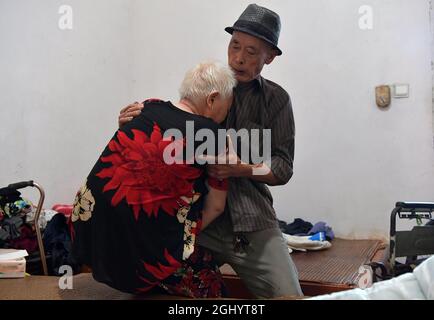 NANCHANG, 8. September 2021 (Xinhua) -- Luo Anmin trägt seine Frau in den Rollstuhl des Dorfes Xuluo im Bezirk Nanchang, ostchinesische Provinz Jiangxi, 5. September 2021. Luo Anmin ist 76 Jahre alt. 2008 litt seine Frau Wan Zhaolian an Hirntumor und verlor leider das Bewusstsein, aber Luo gab nie auf. Er sprach mit seiner Frau und gab ihr jeden Tag Massagen, in der Hoffnung, dass es ihr eines Tages besser gehen könnte. Nach drei Jahren liebevoller Fürsorge geschah das Wunder. 2011 erlangte Wan Zhaolian wieder das Bewusstsein, was Luo mehr Hoffnung gab, obwohl sie immer noch nicht sprechen und gehen konnte. Luo sagte er Stockfoto