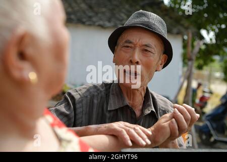 NANCHANG, 8. September 2021 (Xinhua) -- Luo Anmin spricht mit seiner Frau im Hof des Dorfes Xuluo im Bezirk Nanchang, Provinz Jiangxi, Ostchina, 5. September 2021. Luo Anmin ist 76 Jahre alt. 2008 litt seine Frau Wan Zhaolian an Hirntumor und verlor leider das Bewusstsein, aber Luo gab nie auf. Er sprach mit seiner Frau und gab ihr jeden Tag Massagen, in der Hoffnung, dass es ihr eines Tages besser gehen könnte. Nach drei Jahren liebevoller Fürsorge geschah das Wunder. 2011 erlangte Wan Zhaolian wieder das Bewusstsein, was Luo mehr Hoffnung gab, obwohl sie immer noch nicht sprechen und gehen konnte. Luo sagte, er liebe es Stockfoto