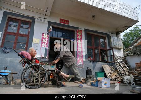 NANCHANG, 8. September 2021 (Xinhua) -- Luo Anmin bringt seine Frau auf den Hof, um im Dorf Xuluo im Bezirk Nanchang, ostchinesische Provinz Jiangxi, am 5. September 2021 Sonne zu baden. Luo Anmin ist 76 Jahre alt. 2008 litt seine Frau Wan Zhaolian an Hirntumor und verlor leider das Bewusstsein, aber Luo gab nie auf. Er sprach mit seiner Frau und gab ihr jeden Tag Massagen, in der Hoffnung, dass es ihr eines Tages besser gehen könnte. Nach drei Jahren liebevoller Fürsorge geschah das Wunder. 2011 erlangte Wan Zhaolian wieder das Bewusstsein, was Luo mehr Hoffnung gab, obwohl sie immer noch nicht sprechen und gehen konnte. Stockfoto