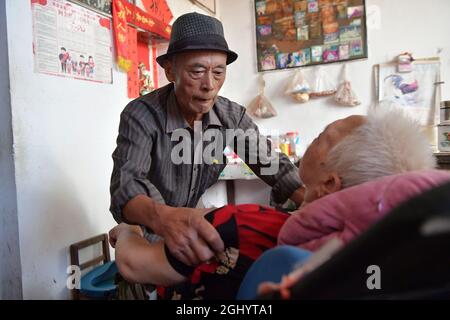 NANCHANG, 8. September 2021 (Xinhua) -- Luo Anmin bereitet sich darauf vor, seine Frau mit nach draußen zu nehmen, um im Dorf Xuluo im Bezirk Nanchang, ostchinesische Provinz Jiangxi, am 5. September 2021 Sonne zu baden. Luo Anmin ist 76 Jahre alt. 2008 litt seine Frau Wan Zhaolian an Hirntumor und verlor leider das Bewusstsein, aber Luo gab nie auf. Er sprach mit seiner Frau und gab ihr jeden Tag Massagen, in der Hoffnung, dass es ihr eines Tages besser gehen könnte. Nach drei Jahren liebevoller Fürsorge geschah das Wunder. 2011 erlangte Wan Zhaolian wieder das Bewusstsein, was Luo mehr Hoffnung gab, obwohl sie immer noch nicht sprechen konnte Stockfoto